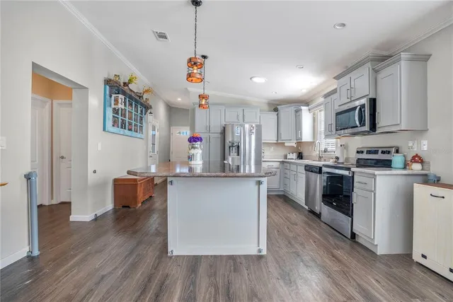a kitchen with stainless steel appliances granite countertop a refrigerator a stove top oven a sink dishwasher and white cabinets with wooden floor
