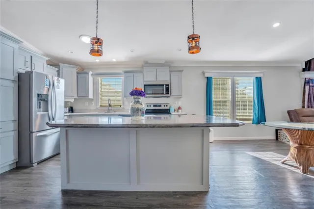 a kitchen with stainless steel appliances granite countertop a refrigerator a sink dishwasher a stove and a dining table with wooden floor