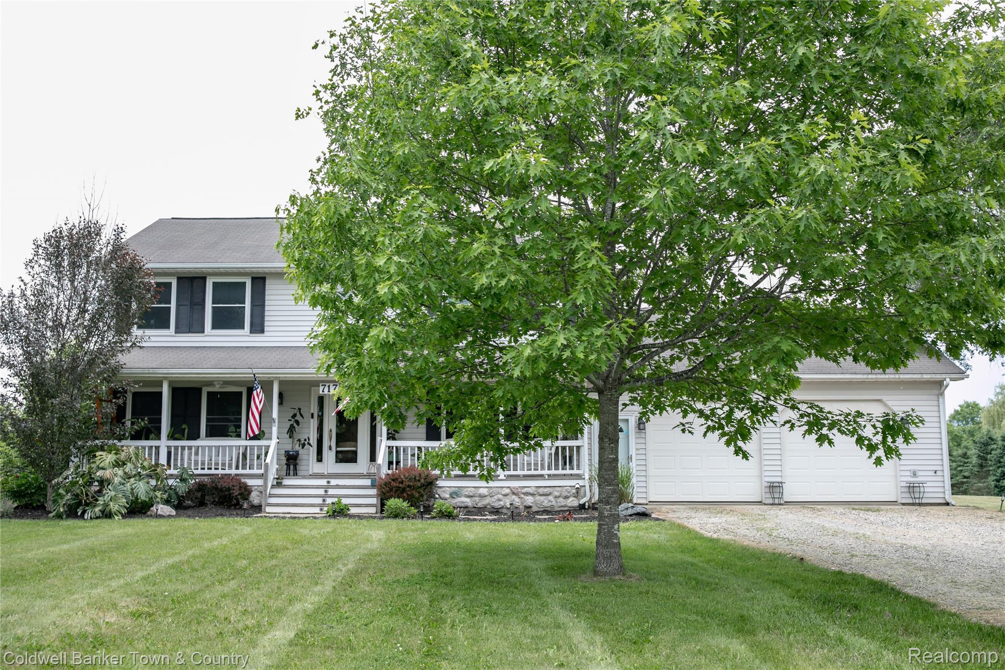 717 North Youngs Road Attica, MI 48412 - Photo 3 of 87 Two-story residence featuring white siding, a covered front porch with white railings, stone detailing on the porch foundation, dark window shutters, and a two-car garage with white doors