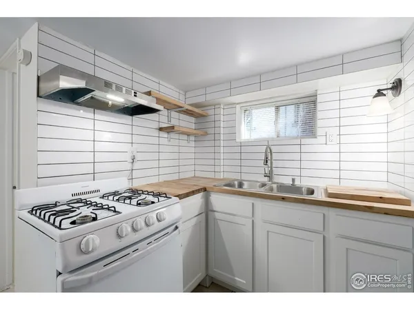 a white kitchen with a stove a sink and wooden floor