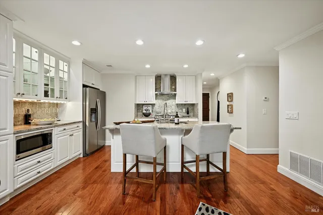 a kitchen with stainless steel appliances kitchen island granite countertop a refrigerator a stove a sink a dining table and chairs with wooden floor