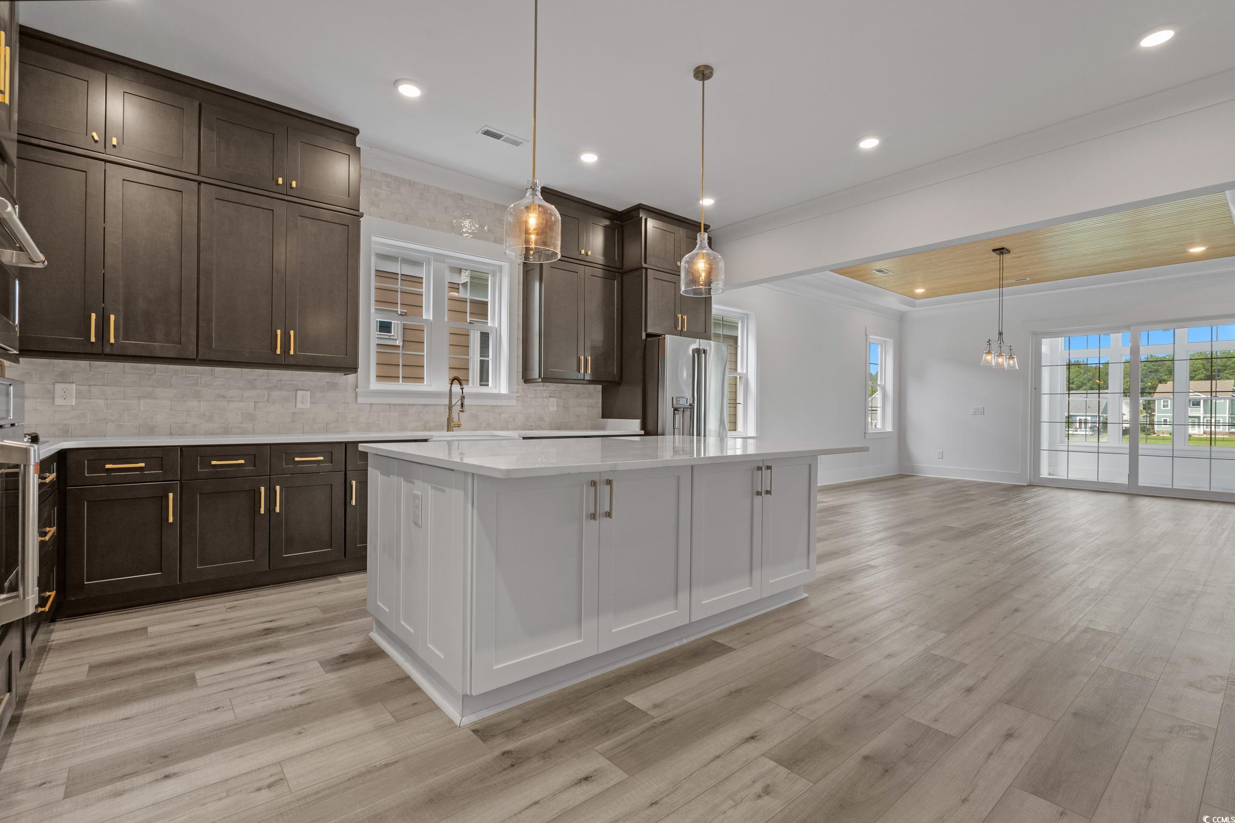921 Crystal Water Way Myrtle Beach, SC 29579 - Photo 9 of 36 Kitchen featuring white cabinets, decorative backsplash, hanging light fixtures, dark brown cabinets, and crown molding