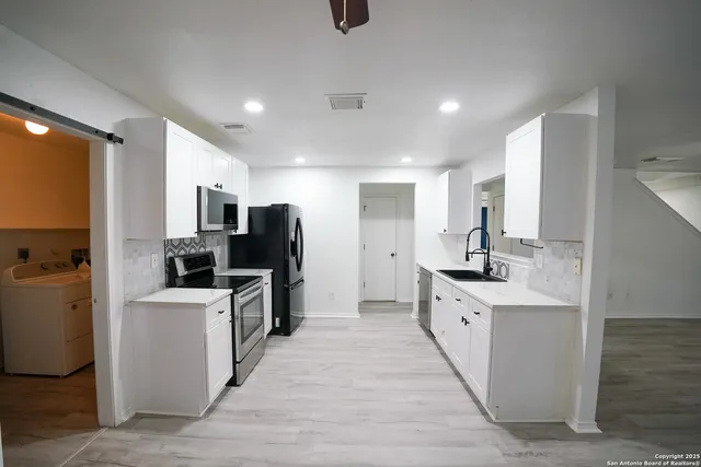 a large kitchen with stainless steel appliances a sink a stove top oven a counter space and cabinets