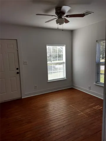 a view of an empty room with wooden floor fridge and a window