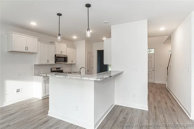 a kitchen with stainless steel appliances kitchen island a refrigerator a sink dishwasher a stove and white cabinets with wooden floor