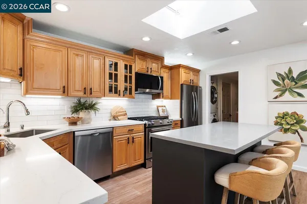 a open kitchen with stainless steel appliances granite countertop a stove top oven a couches and a dining table with wooden floor