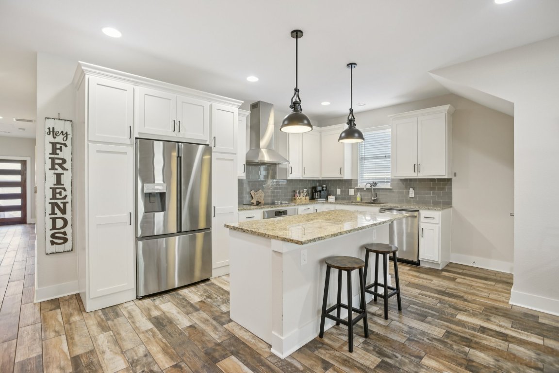 1206 Deloney Street, Unit B Austin, TX 78721 - Photo 2 of 39 Kitchen featuring appliances with stainless steel finishes, a kitchen bar, light stone counters, a center island, and white cabinetry
