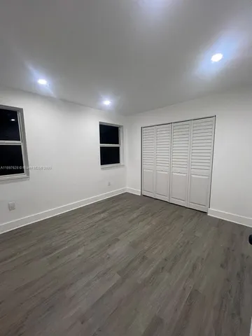 a view of an empty room with wooden floor and a kitchen