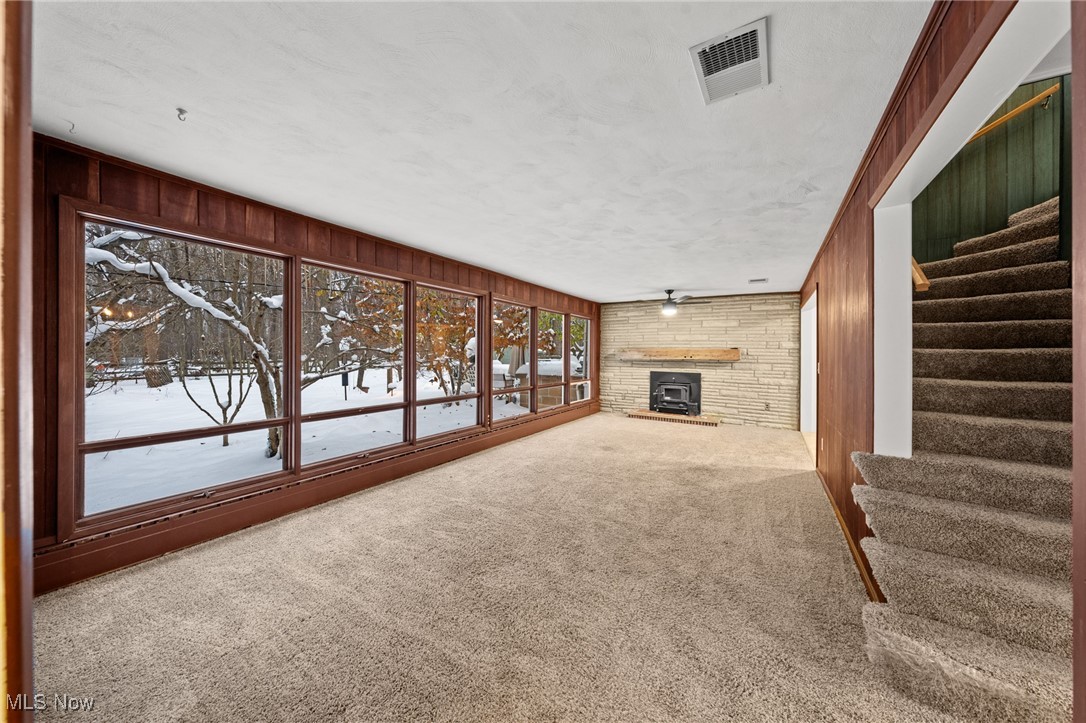 9513 Booth Road Willoughby, OH 44094 - Photo 16 of 45 Unfurnished living room with carpet flooring, a wood stove, wooden walls, and a textured ceiling