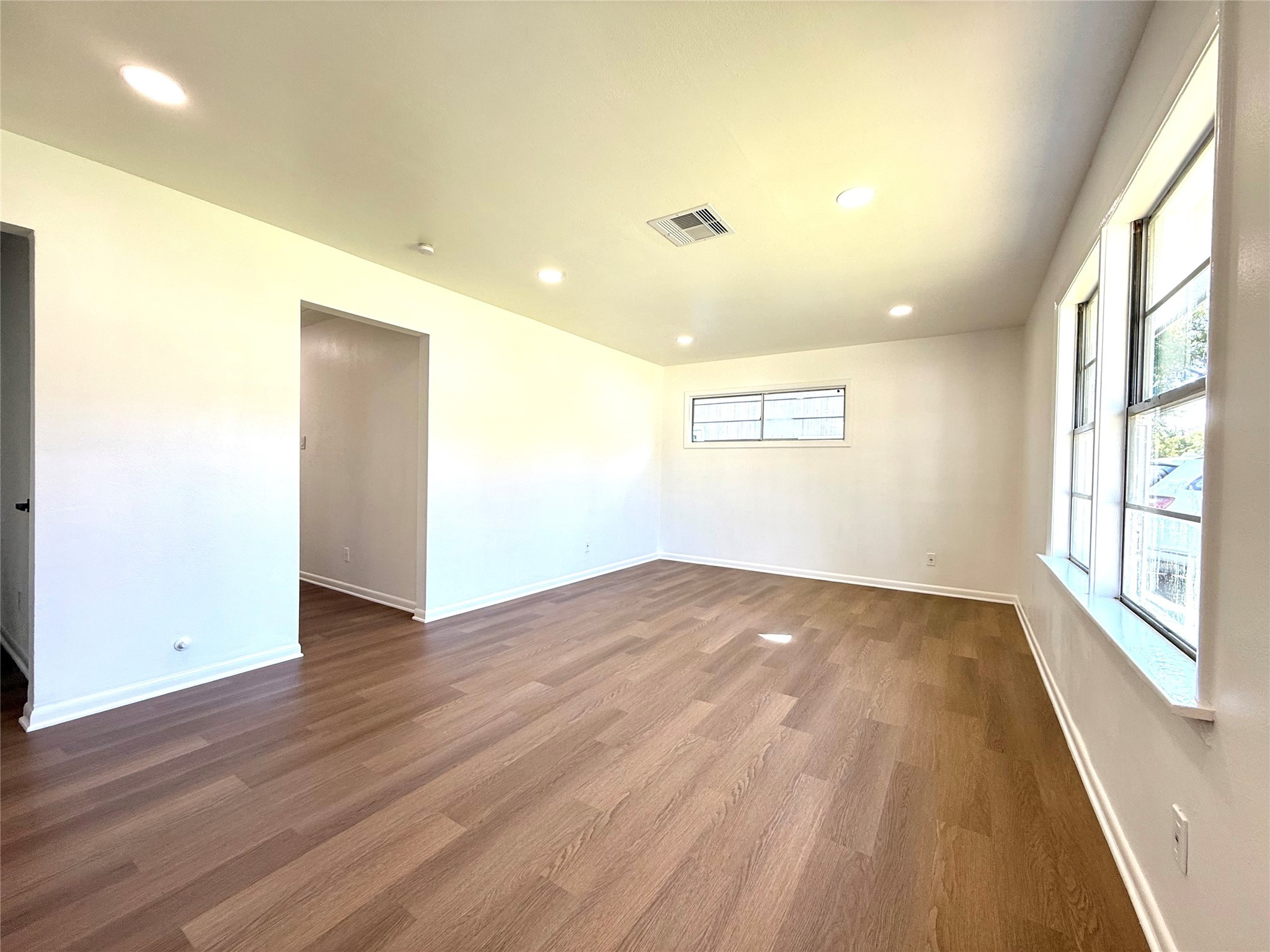129 Chestnut Street Lake Jackson, TX 77566 - Photo 2 of 20 This room features bright, natural lighting through large windows, recessed ceiling lights, and stylish wood flooring. The neutral walls offer a fresh, modern touch, creating a spacious and inviting atmosphere.
