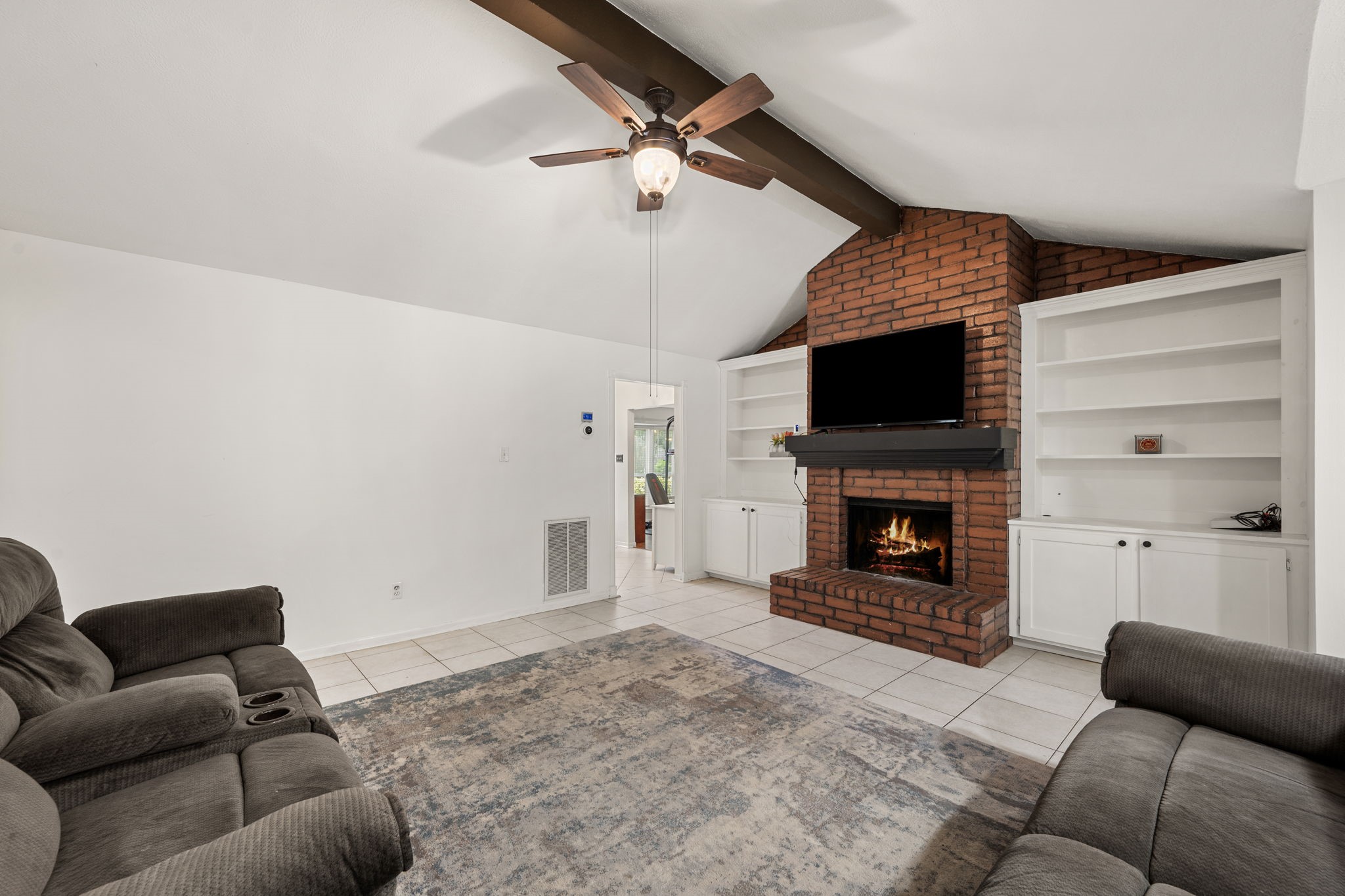 2415 Whispering Springs Drive Spring, TX 77373 - Photo 7 of 28 Spacious living room featuring vaulted ceilings, a stunning floor-to-ceiling brick fireplace, and built-in storage and shelving on both sides of the fireplace, creating a warm and functional focal point for the home.