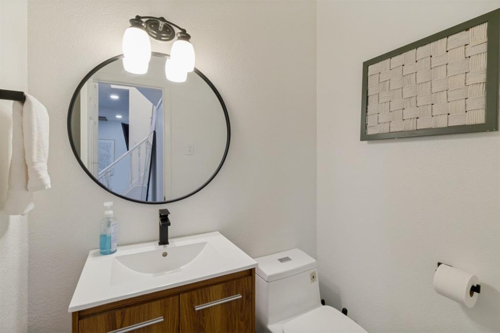3904 Rawlins Street, Unit 112 Dallas, TX 75219 - Photo 14 of 15 Bathroom featuring a wood-finish vanity with a white integrated sink, a matte black faucet, and a circular black-framed mirror