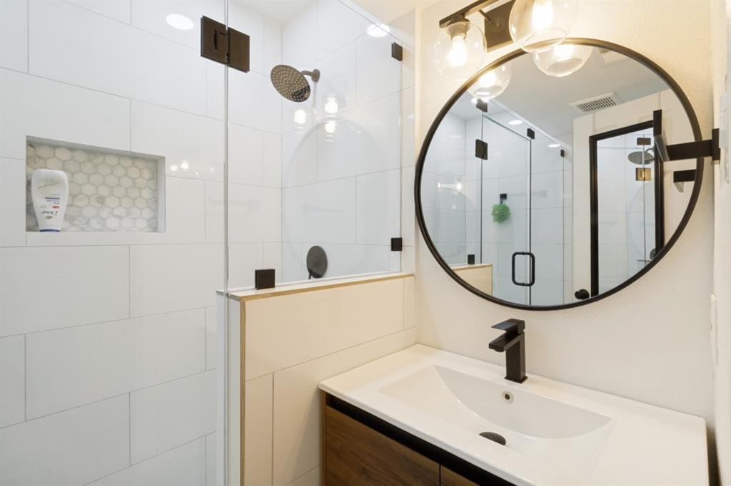 3904 Rawlins Street, Unit 112 Dallas, TX 75219 - Photo 10 of 15 Modern bathroom featuring a wood-finish vanity with an integrated sink, matte black faucet, and a circular mirror with a black frame