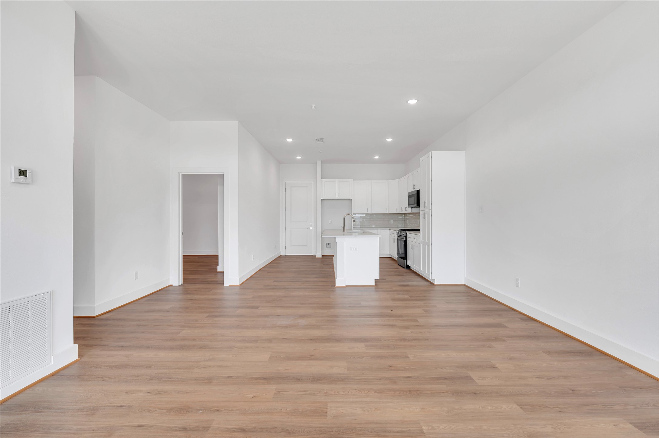 119 Kirby Road, Unit 5205 Seabrook, TX 77586 - Photo 37 of 46 Open-concept living area with sleek hardwood floors and a modern kitchen featuring white cabinetry, stainless steel appliances, and a central island.