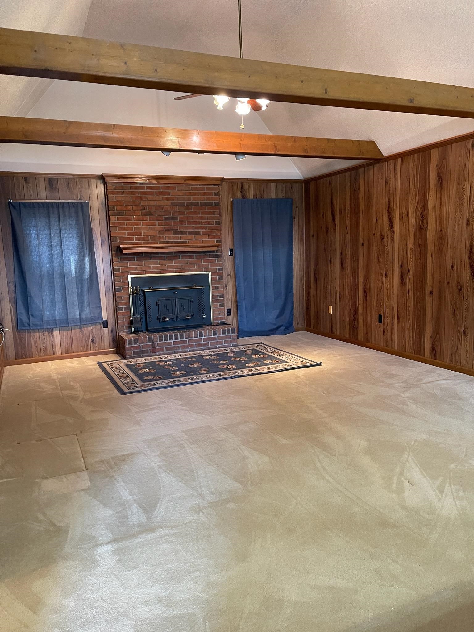 1199 McQuiston Road Brighton, TN 38011 - Photo 8 of 16 Unfurnished living room featuring beamed ceiling, wood walls, and carpet floors