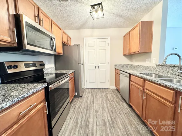 a kitchen with stainless steel appliances granite countertop wooden cabinets a stove top oven a sink and dishwasher with wooden floor
