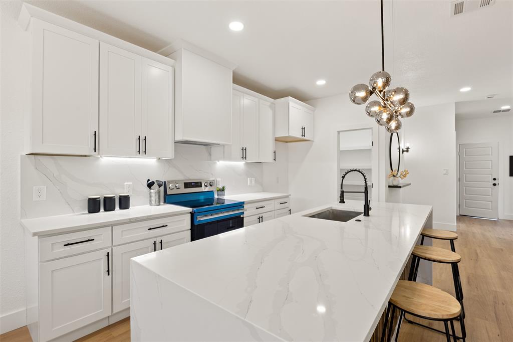 3524 Spring Avenue Dallas, TX 75210 - Photo 8 of 29 Kitchen with stainless steel electric range oven, light wood finished floors, white cabinetry, light stone counters, and a center island with sink