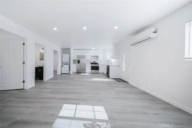 an empty room with wooden floor kitchen view and windows