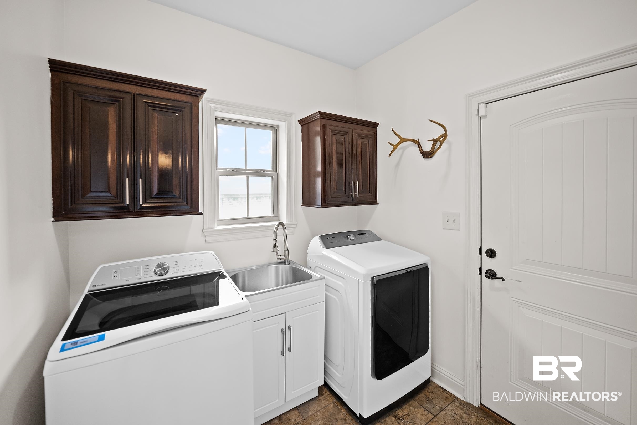 313 Pecan Ridge Boulevard Fairhope, AL 36532 - Photo 29 of 51 Laundry room featuring dark wood-finish cabinetry, a utility sink with a stainless steel faucet, and tile flooring