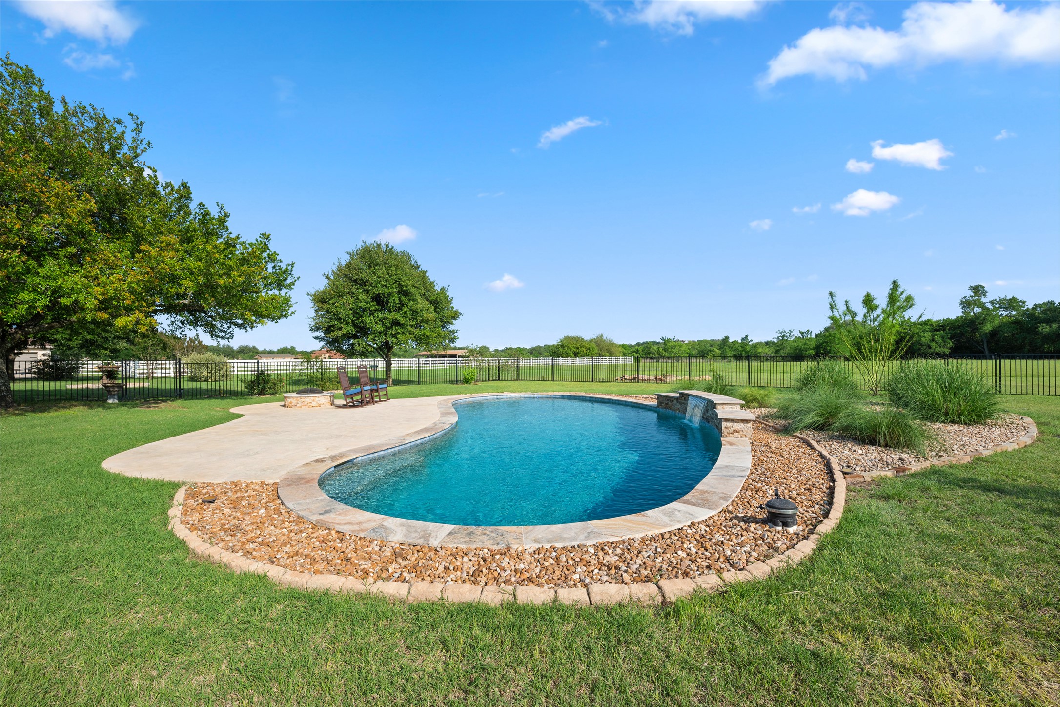 266 Courtnee's Way Georgetown, TX 78626 - Photo 30 of 40 Freeform swimming pool with a waterfall feature, surrounded by a concrete patio and a stone-edged landscape bed with decorative gravel