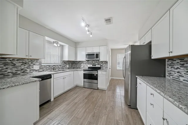 a kitchen with granite countertop a refrigerator oven a sink dishwasher and white cabinets with wooden floor