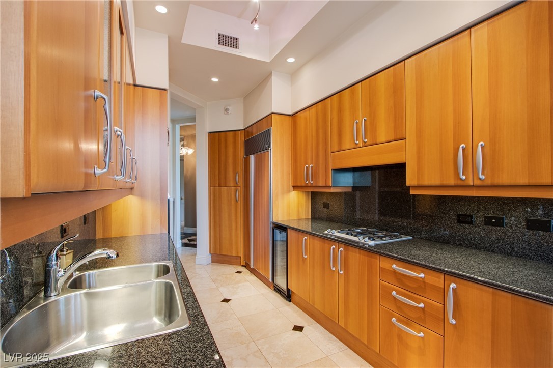 2857 Paradise Road, Unit 206 Las Vegas, NV 89109 - Photo 21 of 31 Kitchen featuring brown cabinetry, recessed lighting, dark stone counters, beverage cooler, and backsplash