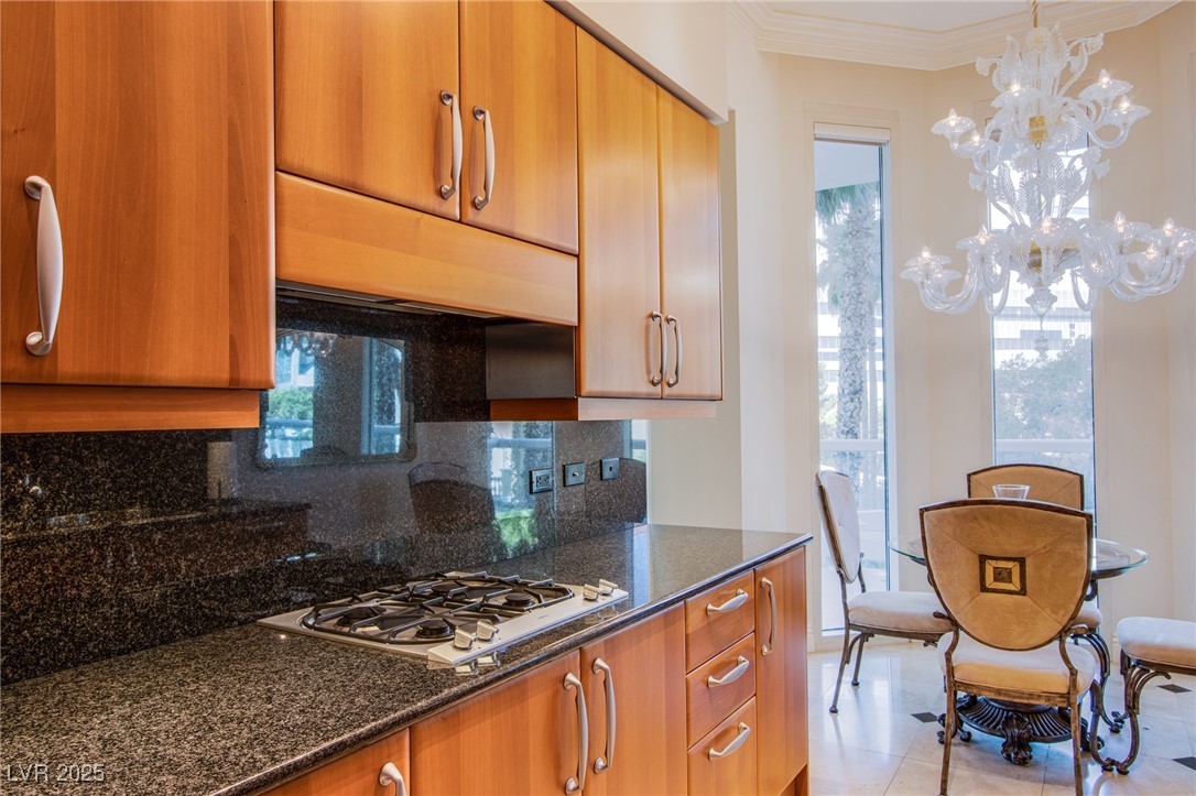 2857 Paradise Road, Unit 206 Las Vegas, NV 89109 - Photo 23 of 31 Kitchen featuring decorative backsplash, dark stone countertops, under cabinet range hood, hanging light fixtures, and white gas stovetop