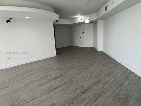 a view of an empty room with wooden floor and a window