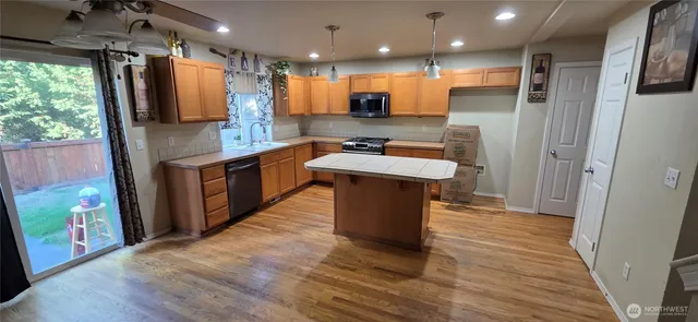 a kitchen with stainless steel appliances granite countertop a refrigerator a sink dishwasher a stove and white countertops with wooden floor