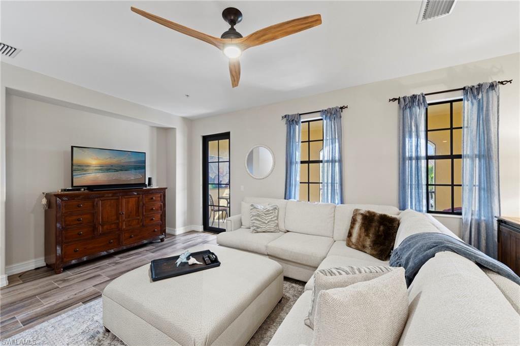 9076 Rialto Street, Unit 6204 Naples, FL 34113 - Photo 7 of 50 Spacious living area featuring wood-finish flooring, a modern ceiling fan, and multiple windows with dark frames. NEW TILE FLOOR (2018)