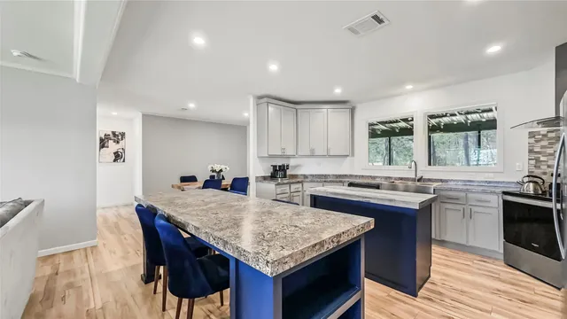 a kitchen with granite countertop kitchen island stainless steel appliances sink stove dining table and chairs