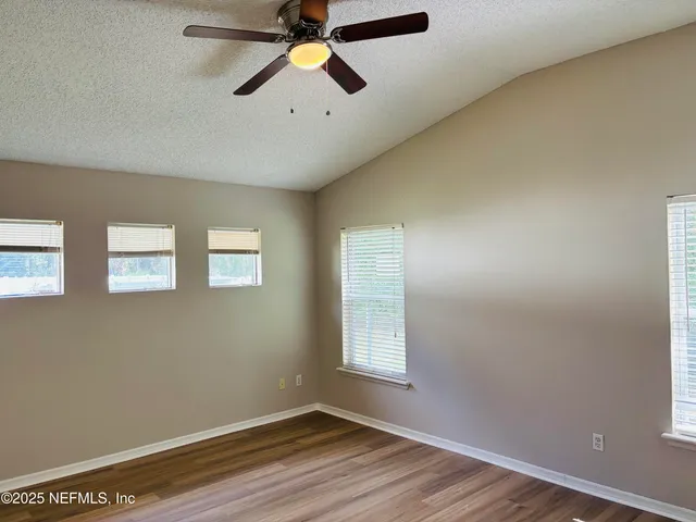 an empty room with wooden floor ceiling fan and windows