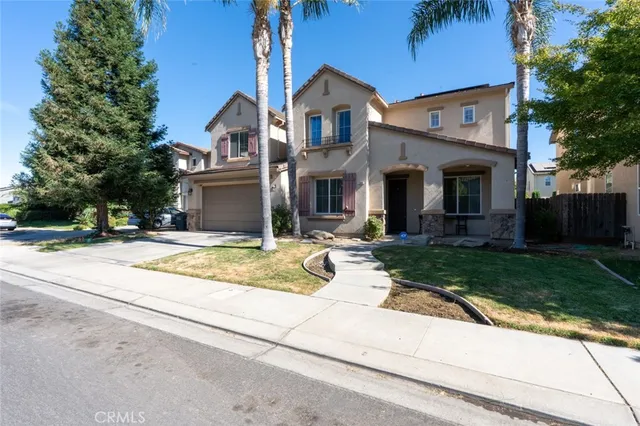 a view of a white house with a yard plants and a large tree
