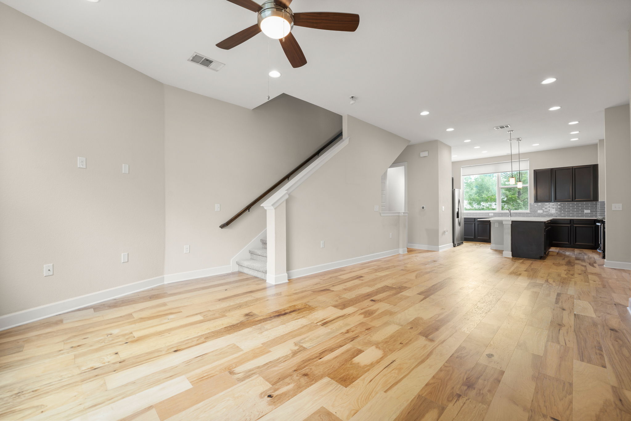 4403 Swift Path Austin, TX 78741 - Photo 8 of 32 Spacious living area featuring light wood-finish flooring, a contemporary ceiling fan, recessed lighting, and a staircase with white risers and a dark wood handrail