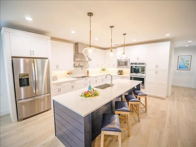 a kitchen with stainless steel appliances kitchen island granite countertop a refrigerator a sink and white cabinets