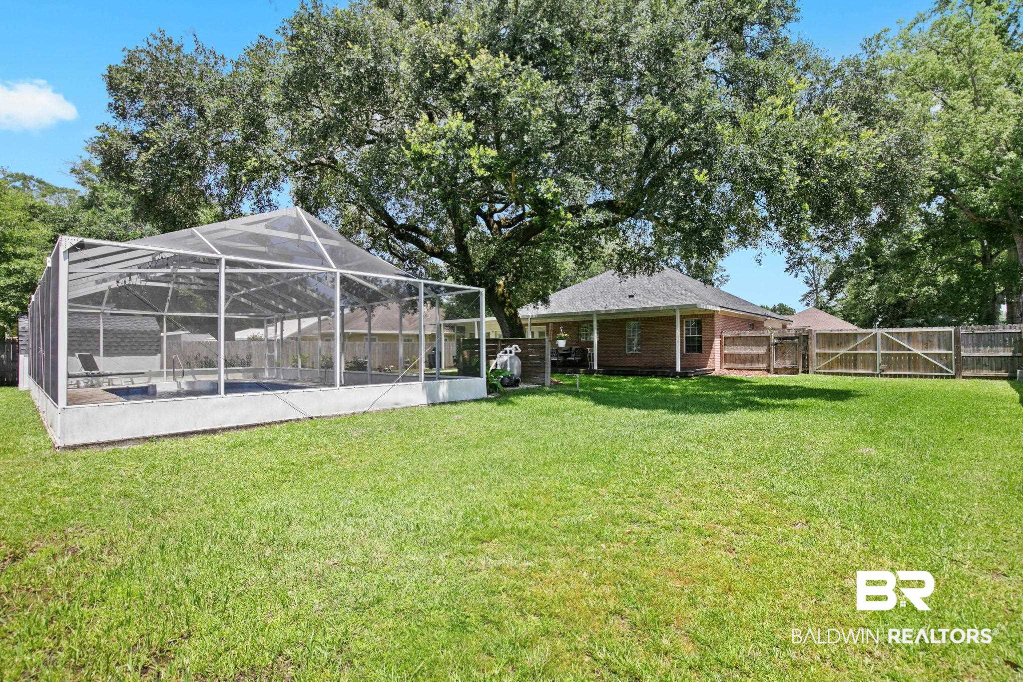 520 Juniper Place Drive Foley, AL 36535 - Photo 29 of 35 Expansive backyard featuring a screened-in swimming pool enclosure, large mature trees, a manicured lawn, and a wooden privacy fence
