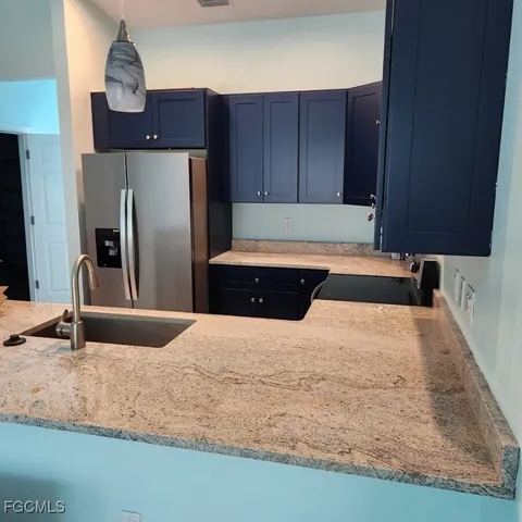 a kitchen with kitchen island granite countertop a refrigerator a stove and a sink with wooden cabinets