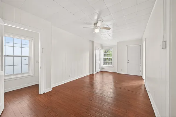 an empty room with wooden floor chandelier fan and windows
