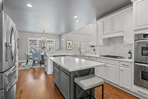 a open kitchen with stainless steel appliances granite countertop a stove top oven a sink dishwasher and white cabinets with wooden floor