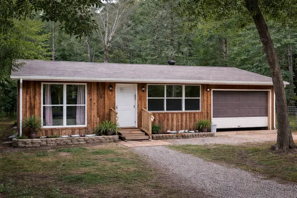 a front view of a house with a yard and glass top table and chairs under an umbrella