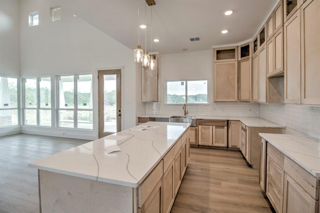 117 Mustang Springs Circle Sunset, TX 76270 - Photo 12 of 40 Kitchen with wood finished floors, pendant lighting, a center island, light brown cabinets, and light stone counters