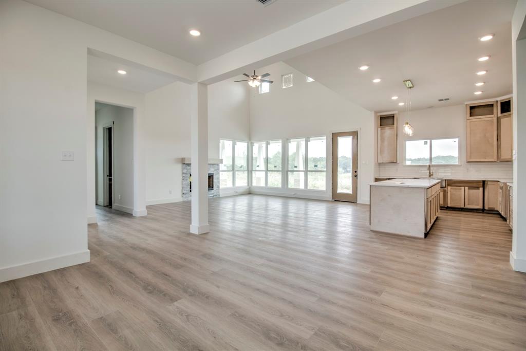 117 Mustang Springs Circle Sunset, TX 76270 - Photo 7 of 40 Unfurnished living room with recessed lighting, a towering ceiling, light wood-style flooring, a fireplace, and a ceiling fan