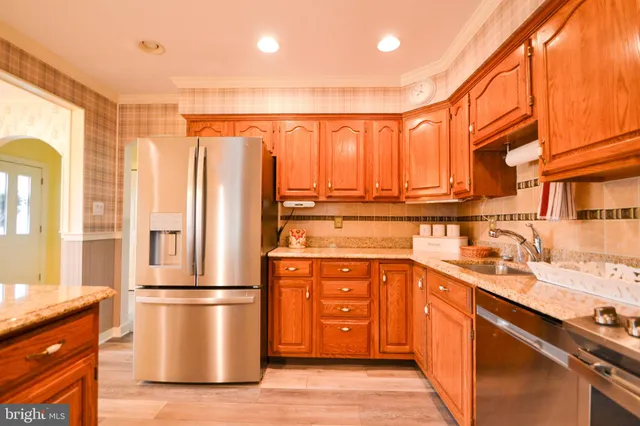 a kitchen with stainless steel appliances granite countertop a refrigerator a sink dishwasher and wooden cabinets with wooden floor