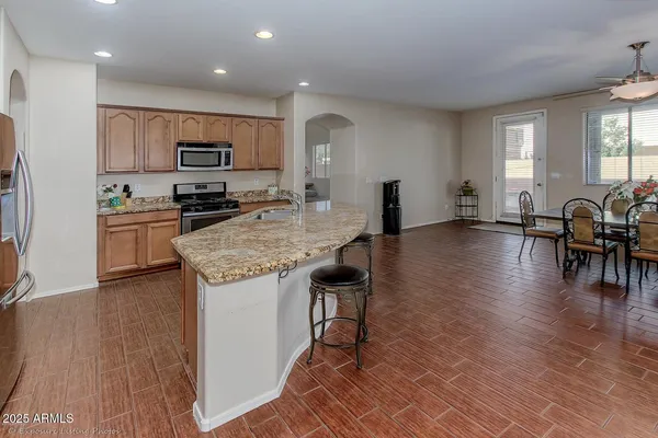 a kitchen with stainless steel appliances granite countertop a stove top oven a sink a dining table and chairs with wooden floor