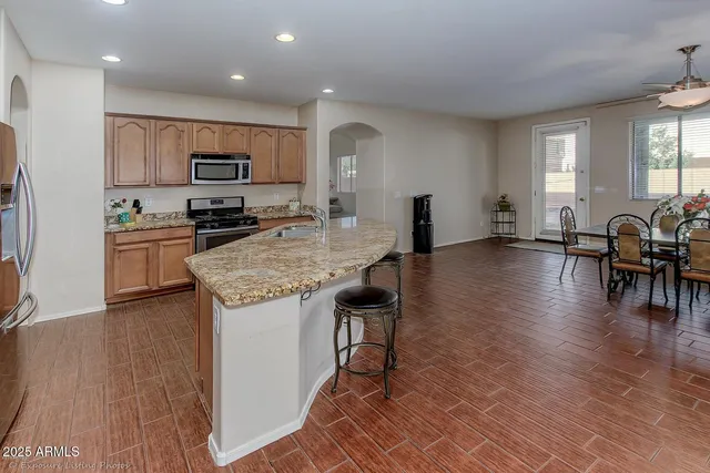 a kitchen with stainless steel appliances granite countertop a stove top oven a sink a dining table and chairs with wooden floor