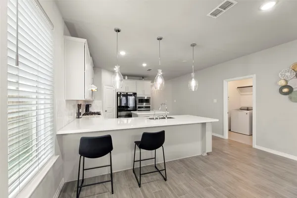 a kitchen with stainless steel appliances kitchen island a sink a stove a refrigerator and white cabinets with wooden floor