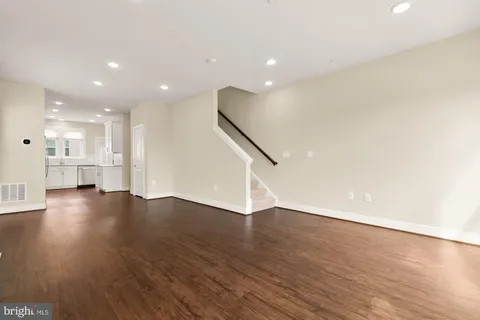 a view of empty room with wooden floor and kitchen