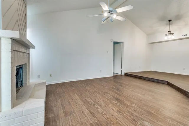 a view of an empty room with wooden floor and a ceiling fan