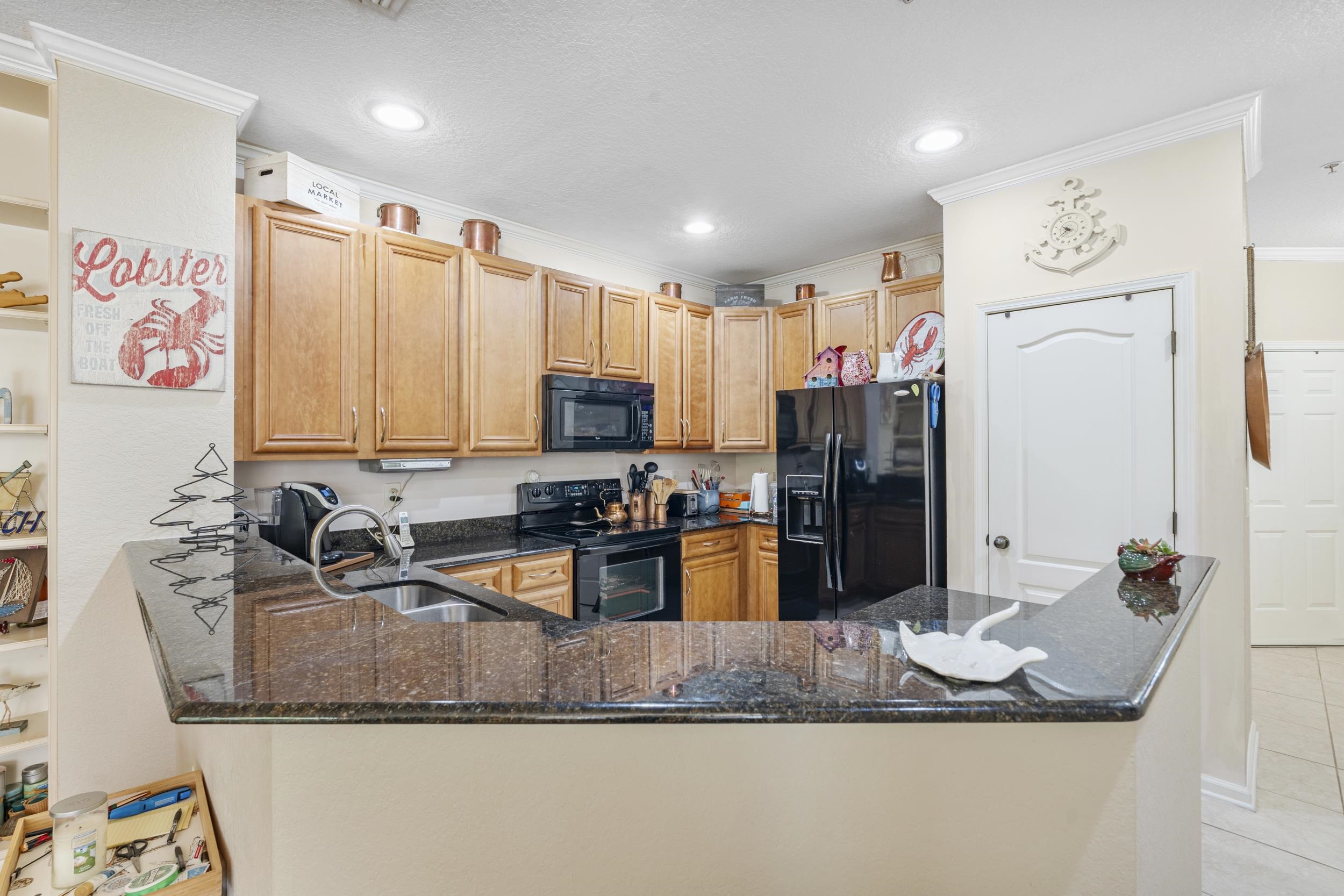 110 Magnolia Crossing Point, Unit 1901 St. Augustine, FL 32086 - Photo 8 of 38 Kitchen featuring black appliances, dark stone countertops, a peninsula, light tile patterned floors, and wood finish cabinetry