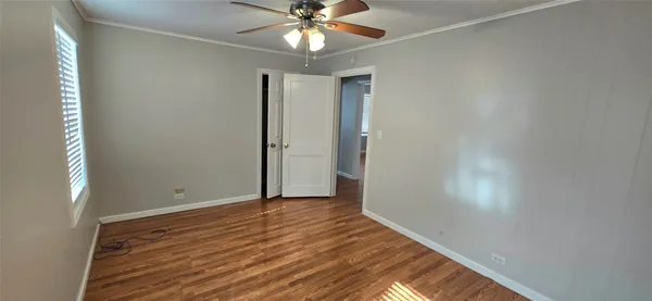 a view of an empty room with wooden floor and a ceiling fan